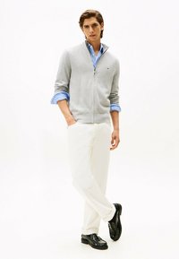 Suéter gris con cierre, camisa azul a rayas debajo, pantalones blancos y zapatos negros. Diseño sencillo con colores y texturas contrastantes.