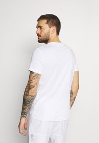 White cotton t-shirt with short sleeves and a round neckline, showing a smooth texture. Back view reveals a fitted design and minimal branding.