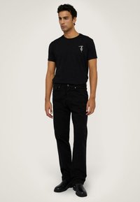 Czarna bawełniana koszulka z krótkim rękawem i grafiką na klatce piersiowej, zestawiona z czarnymi prostymi dżinsami i czarnymi skórzanymi butami.