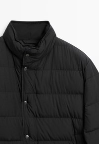 Black puffer jacket with a high collar, snap buttons, and quilted pattern. The material appears soft and water-resistant.