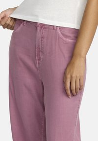 Roze katoenen broek met een relaxte pasvorm, voorzien van zijzakken en subtiele stikdetails. De stof heeft een zachte, matte textuur.