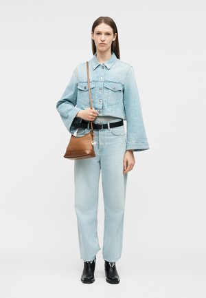 Kvinde iført lyseblå cropped denimjakke og jeans, sort bælte og støvler, holder en brun læder crossbody-taske med logo vedhæng.