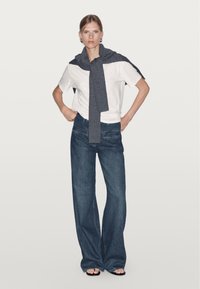 Vit t-shirt, mörkgrå stickad wrap runt axlarna, högmidjade blå vida jeans, svarta sandaler, minimalistisk design, släta texturer.