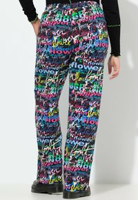 Mønstret bukser i flere farver med blomster og tekst. Stoffet har en glat tekstur, og designet har lysende lyserøde, blå, grønne og gule detaljer.