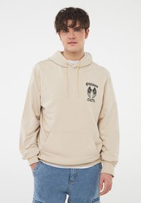 Felpa leggera beige chiaro in misto cotone, con tasca frontale e stampa grafica di ali con la parola "Oblivion". Vestibilità comoda.