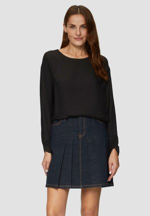 Schwarzes langärmliges Oberteil mit Boot-Ausschnitt, kombiniert mit einem dunklen Jeans-Plisseerock mit sichtbaren Nähten und einer taillierten Taille.