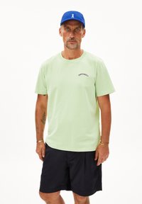 Lichtgroene katoenen t-shirt met geborduurde tekst en korte mouwen, gecombineerd met marineblauwe shorts en een blauwe pet met een wit logo.