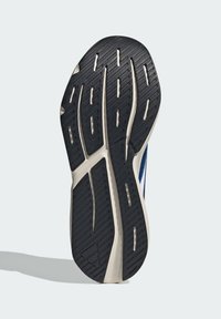 Athletic shoe sole with a black rubber tread pattern, featuring grooves and ridges. The edge is cream-colored, highlighting stability and grip.