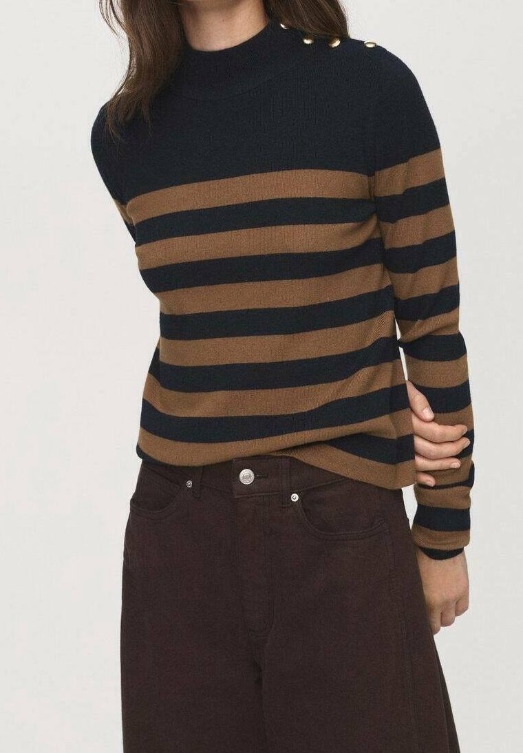 Personne portant un pull à rayures horizontales bleu marine et marron avec des boutons dorés sur l'épaule et un pantalon taille haute marron foncé.