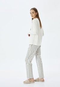 Top blanco de manga larga y pantalones de pijama a rayas grises. Tejido suave, ajuste relajado. La modelo lleva pantuflas beige de felpa. Diseño minimalista.