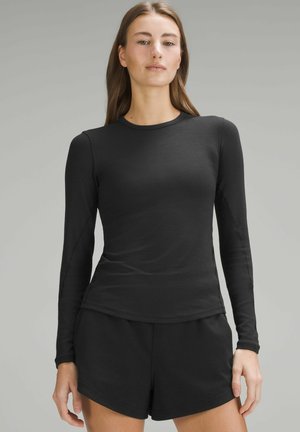 Black long-sleeve top made of smooth fabric with a round neckline. Paired with matching black shorts for a coordinated look.