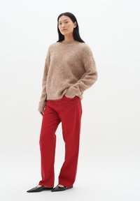 Suéter de un marrón claro y suave con mangas largas, combinado con pantalones rectos rojos brillantes y bailarinas negras de punta. Diseño simple y moderno.