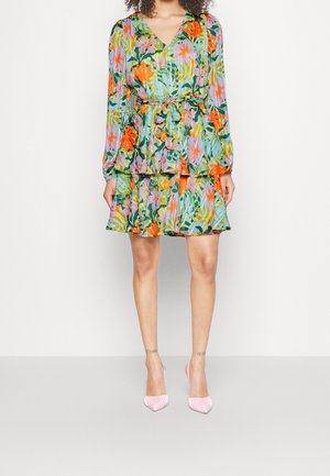 Femme portant une robe fleurie plissée à manches longues avec un col en V et un ourlet à volants, associée à des chaussures à talons hauts rose clair.