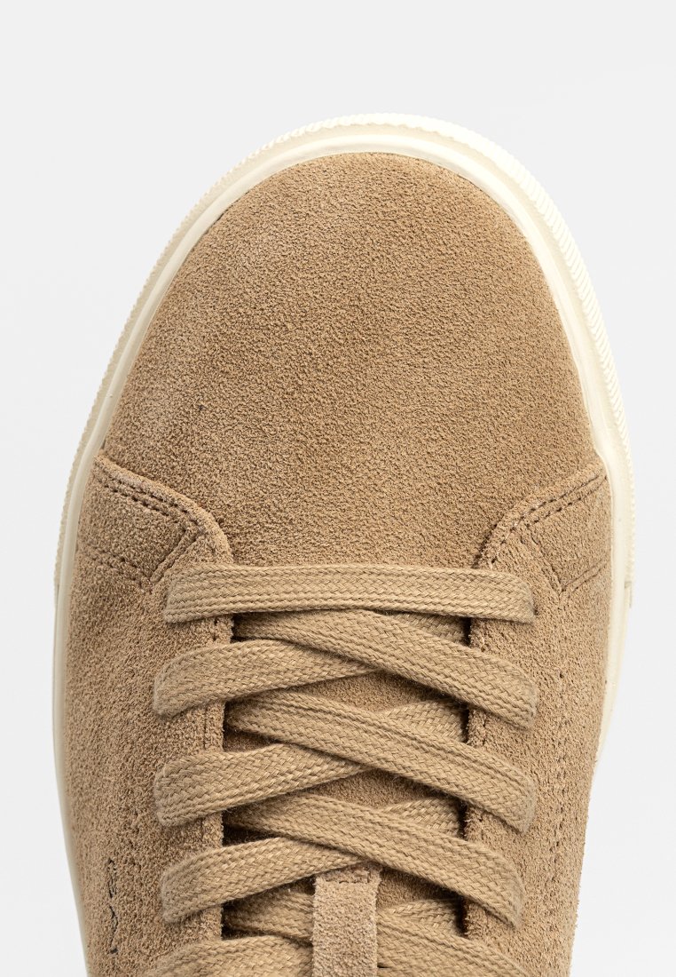 Sneaker in suede color tan con punta tonda, lacci piatti e suola in gomma bianca. Superficie testurizzata con cuciture visibili.