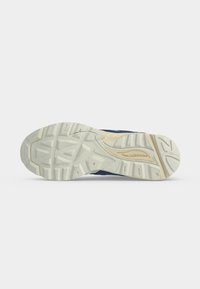 Σόλα μπλε αθλητικού παπουτσιού New Balance με εκρού υφή πέλματος με μοτίβα πρόσφυσης και ανάγλυφο το όνομα της μάρκας στη μεσαία σόλα.