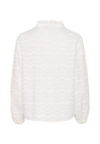 Camicia bianca a maniche lunghe con motivo testurizzato ondulato e piccoli dettagli a pompon. Presenta un colletto a balze e polsini leggermente arricciati.