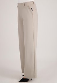 Beige wijde broek van gladde stof, voorzien van een platte voorkant, zijzakken en subtiele branding op de tailleband.