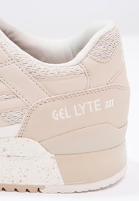 Beige tenisky s texturovaným síťovým svrškem, gumovou podrážkou se skvrnitými akcenty a vyraženým logem "GEL LYTE III" na patě.