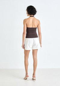 Haut halter ajusté marron associé à un short blanc, mettant en valeur une texture lisse et un design épuré. Le modèle porte des sandales à talons hauts avec des lanières.