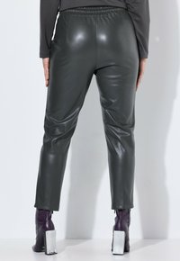 Zelené kalhoty z umělé kůže s elastickým pasem, tapered střihem a hladkou texturou, doplněné fialovými botami na podpatku s bílými akcenty.