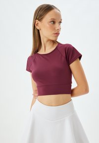 Bordeaux fitted crop top med korte ærmer og rund halsudskæring, lavet af glat stof. Sammen med en hvid høj talje nederdel.