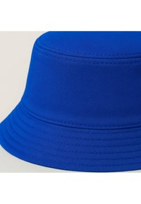 Cappello a secchiello blu con tessuto testurizzato, caratterizzato da una corona rotonda e una tesa ampia e floscia. Sono visibili dettagli di cuciture intorno alla base.