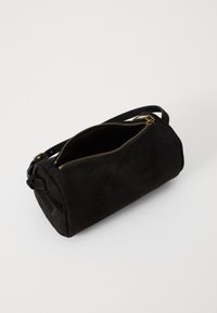 Borsa cilindrica in suede nero con zip superiore, accessori in tonalità oro e manico corto su un lato per un facile trasporto.