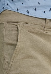 Collared shirt in light blue with small black bird patterns and khaki textured pants featuring front pockets and a straight cut.