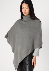 Grå stickad poncho med hög polokrage, med en lös, draperad silhuett och ribbad textur. Förbättrad med en rak kant.