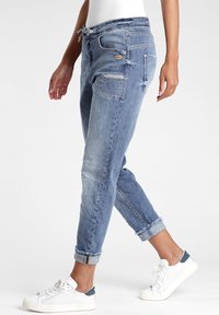 Valaise sininen, farkkutyyppiset jogger-housut, joissa on kapeneva malli, säädettävä nauhavyötärö ja käänteet. Sisältää useita taskuja ja ompeluyksityiskohtia.