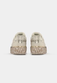 Μπεζ αθλητικά παπούτσια με πλατφόρμα, με μεταλλικά ταμπάκης στη φτέρνα και σόλες με λεοπάρ σχέδιο, απεικονιζόμενα από πίσω σε λευκό φόντο.