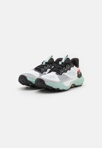 White and black mesh running shoes with a light mint green sole, featuring textured patterns and a logo accent in red.
