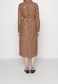 Brunmönstrad klänning med långa ärmar, bälte i midjan och midi-längd. Styld med silverfärgade skor och krage.