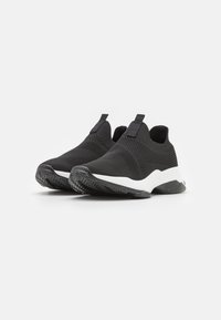 Fekete slip-on sportcipők textúrált hálós felsőrésszel, fehér középsole-lal és gumitalppal, amely diagonál mintázattal rendelkezik. Minimalista dizájn húzókkal.