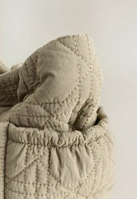 Détail d'un tissu doux et matelassé dans une teinte beige atténuée, mettant en valeur une surface texturée avec des motifs de couture diagonaux.