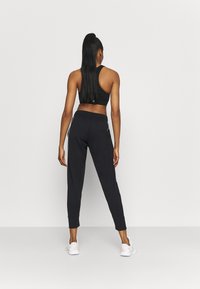 Svart atletisk ensemble bestående av en åtsittande linne och tajta joggers med sidosträck, tillverkade av stretchigt material. Vita sneakers fulländar looken.