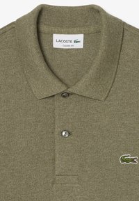 Camisa polo verde oliva con punto texturizado, dos botones y un pequeño logo bordado de cocodrilo en el lado izquierdo del pecho. Diseño de ajuste clásico.