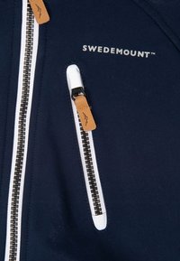 Navy jacket with white accents and a zipper, featuring a tan leather pull tab. "SWEDEMOUNT" logo in silver above the zipper pocket.