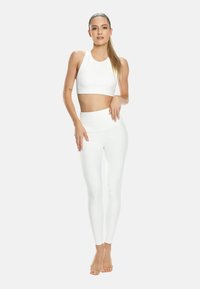 Bílá sportovní podprsenka a legíny s vysokým pasem vyrobené z elastického materiálu. Hrnkový výstřih je zakulacený a legíny jsou přiléhavé bez vzorů.