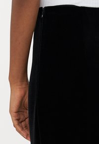 Fekete bársony szoknya sima textúrával és diszkrét oldalsó cipzárral, amely kiemeli a testhez simuló sziluettet és a letisztult vonalakat.