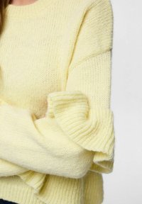 Żółty dziergany sweter z prążkowanymi mankietami i luźnym krojem. Tekstura jest cienka, miękka i lekko puszysta z subtelnym połyskiem.