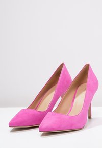 Růžové semišové lodičky na vysokém podpatku se špičatou špičkou a štíhlým stiletto podpatkem. Vnitřní podšívka je béžová a hladká na dotek.