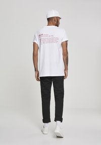 White cotton t-shirt with red text on the back defining "skrrt." Worn with black pants and white sneakers, featuring rolled cuffs and a cap.