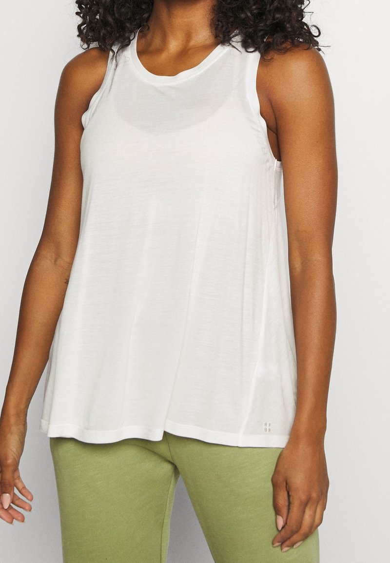 Bílá bezramínková tílko s volným střihem, vyrobené z lehkého materiálu, s kulatým výstřihem a jemnými švy.