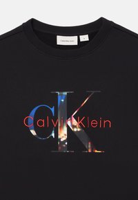 Felpa nera con un grande design grafico recante la scritta "Calvin Klein" in rosso e "CK" in un pattern astratto multicolore. Collo rotondo.
