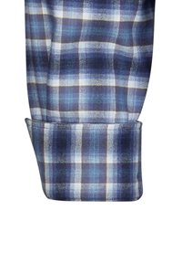 Polsino della camicia di flanella a quadri blu e bianchi, con un motivo a quadri in diverse tonalità di blu. Texture morbida e dettaglio delle maniche arrotolate visibile.
