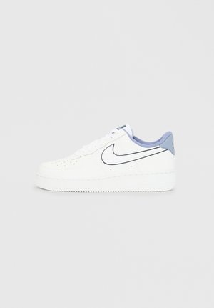 Zapatilla Nike blanca de corte bajo con perforaciones, swoosh con contorno negro y cuello azul claro sobre fondo gris liso.