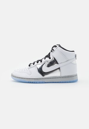 Baskets montantes blanches avec des lacets noirs, un swoosh Nike noir métallique brillant et une semelle translucide bleu glacé sur fond blanc.