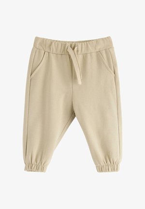 Beige barnbyxor med elastisk midja, dragsko, sidofickor och elastiska muddar på vit bakgrund.