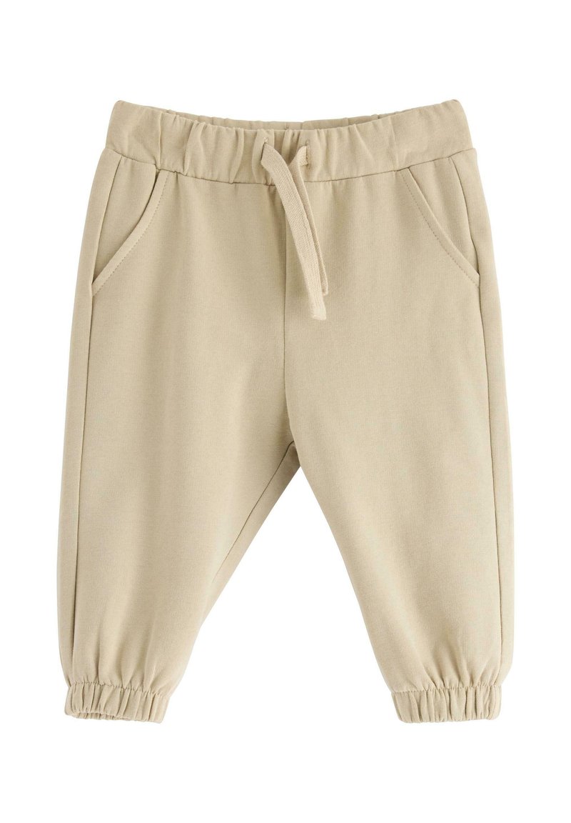 Beige barnbyxor med elastisk midja, dragsko, sidofickor och elastiska muddar på vit bakgrund.